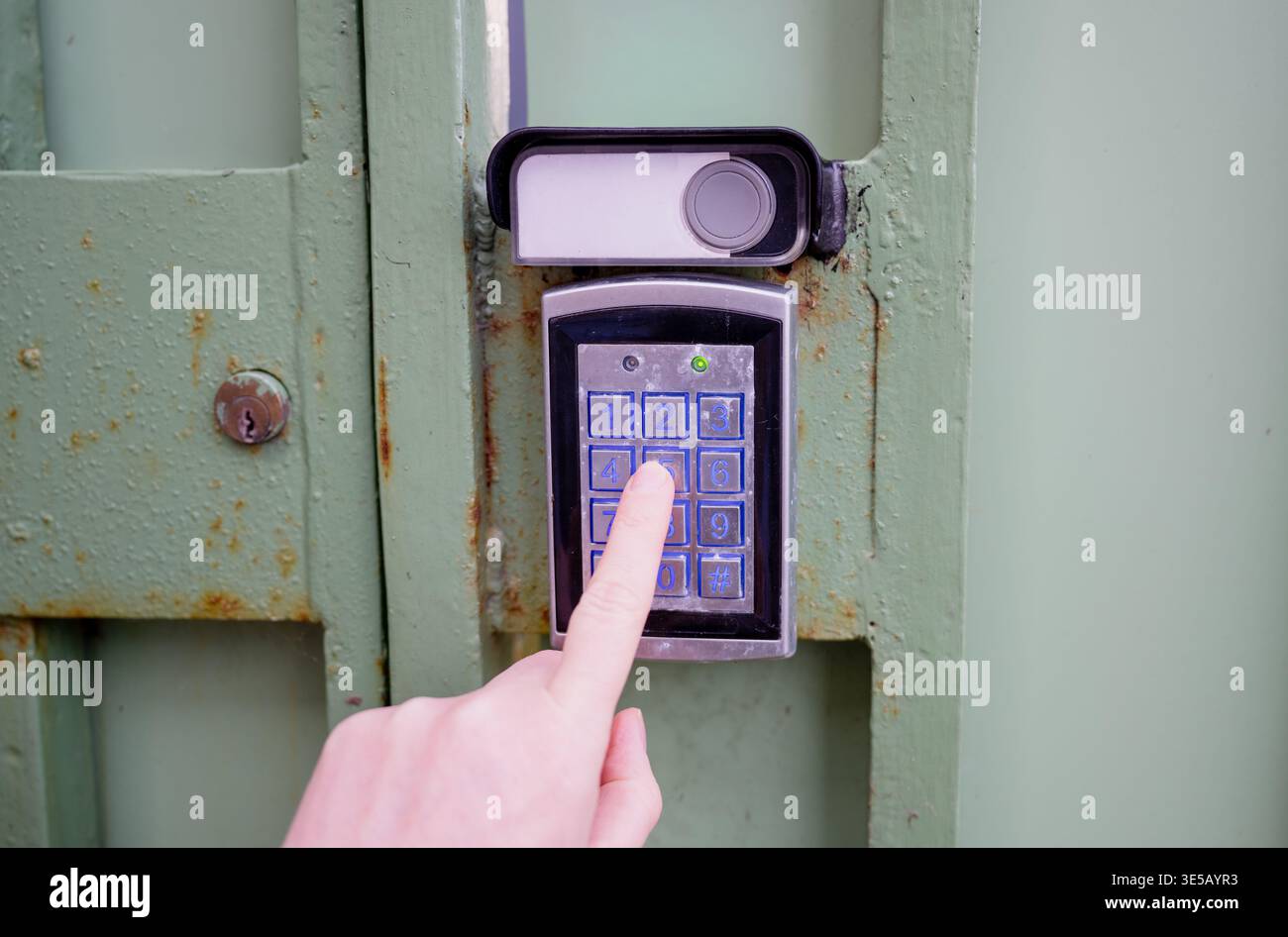 Person entering security code on electronic keypad access control system at metal gate with secure entry concept Stock Photo