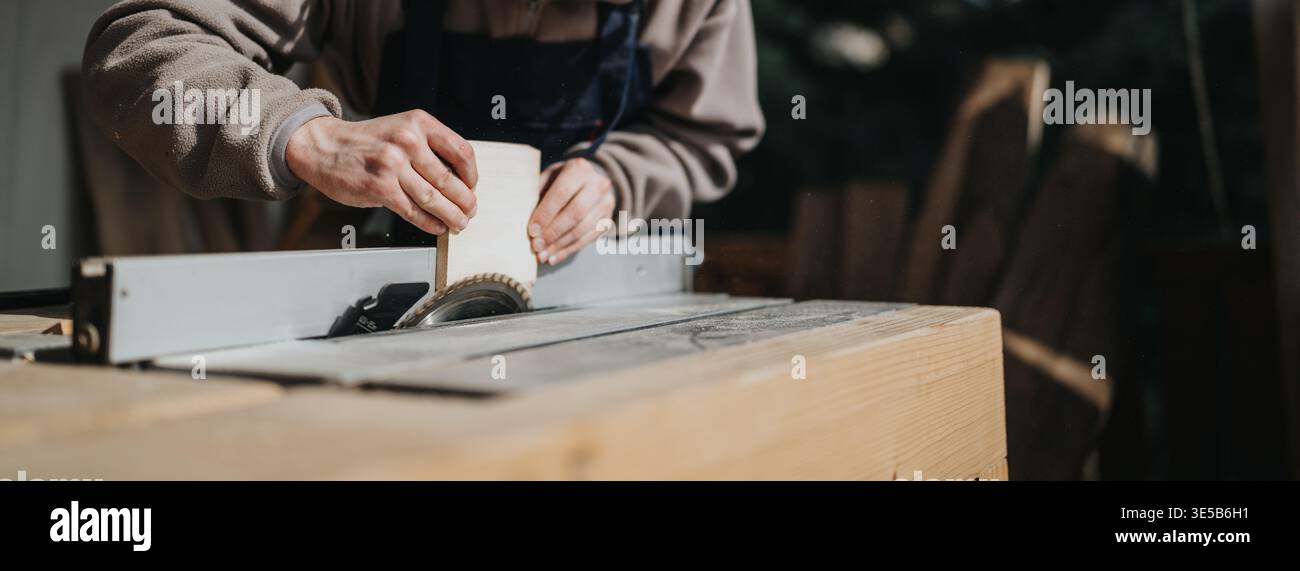 Craftsman cutting wood on a table saw in a workshop using hand-guided technique Stock Photo