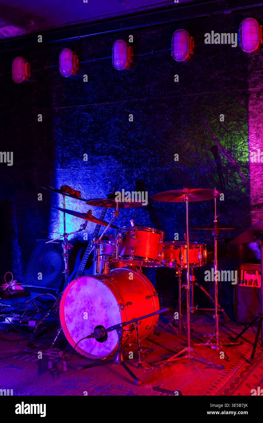 Drum kit set up on stage, bathed in blue and red neon lighting, ready for a live performance Stock Photo