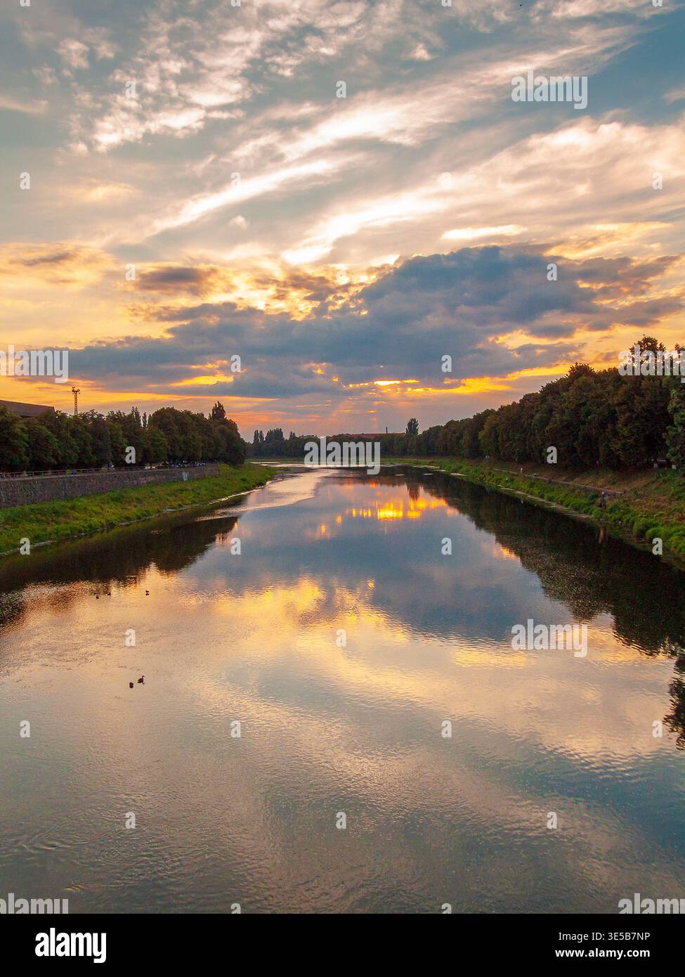 uzhhorod, ukraine - 31 jun, 2007: view of the river uzh at sunset. lush trees on the grassy shore in evening city scenery. cloudy sky reflecting on th Stock Photo