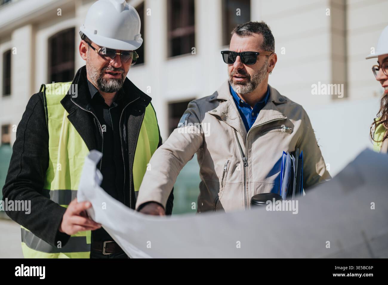 Construction project managers reviewing blueprints at a building site ...