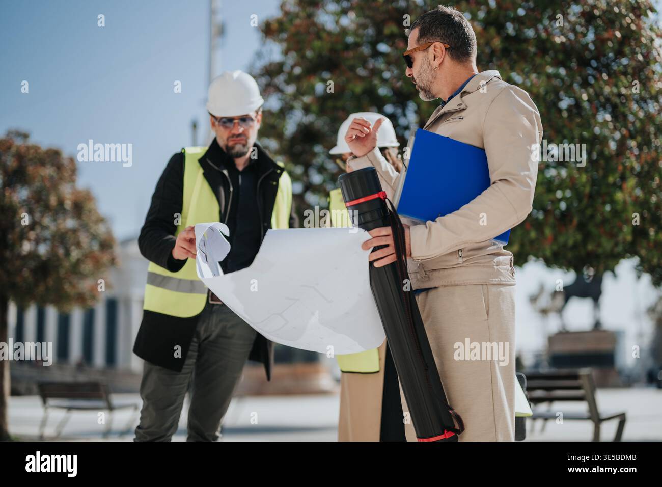 Construction engineers reviewing blueprints on site while discussing urban project plans Stock Photo