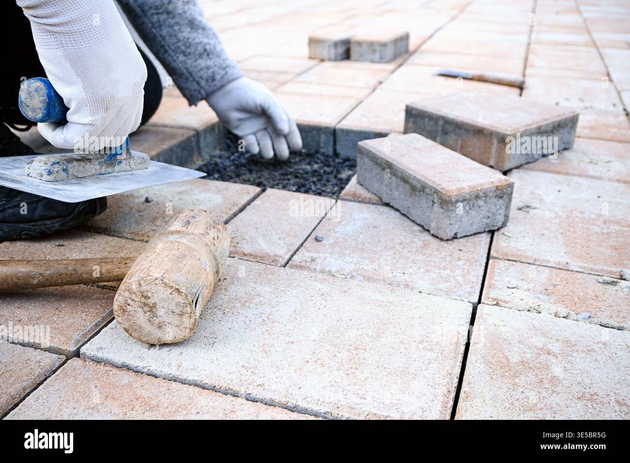Worker is carefully placing paving stones on a prepared gravel base for a new patio. Stock Photo