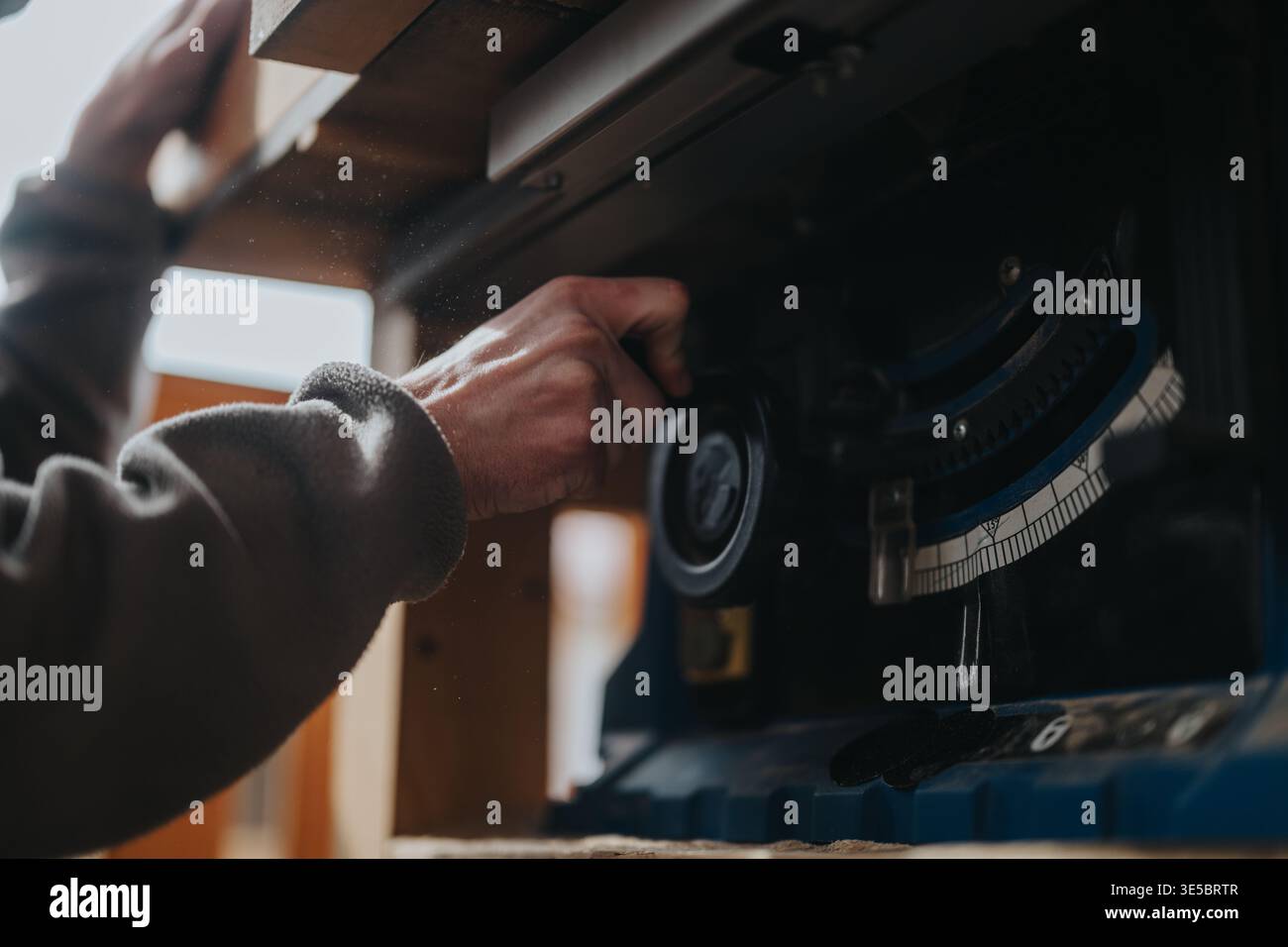 Woodworker adjusting table saw angle with hand in a dusty workshop setting for precision cutting Stock Photo
