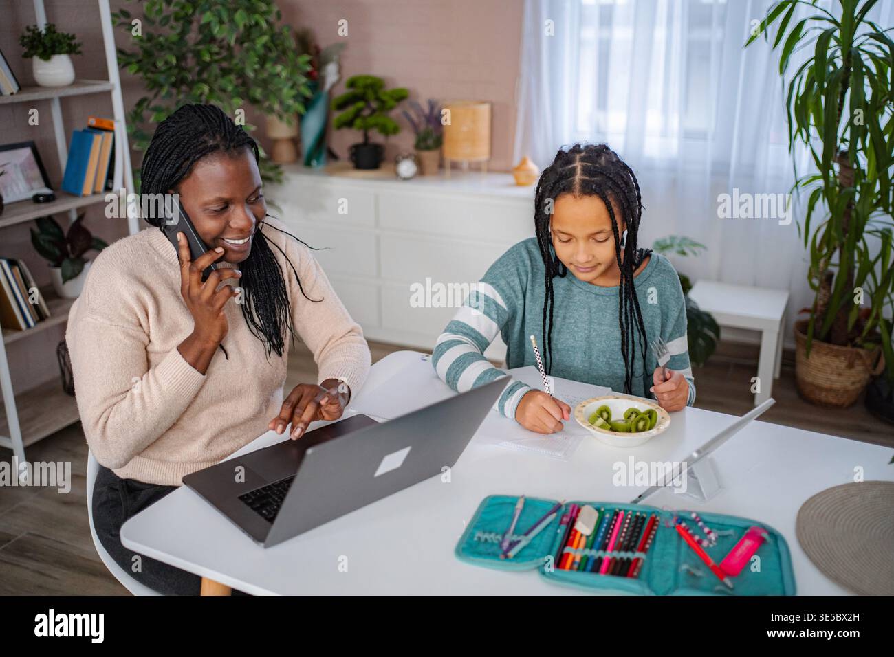 Mother talking on phone and using laptop while daughter studying Stock Photo