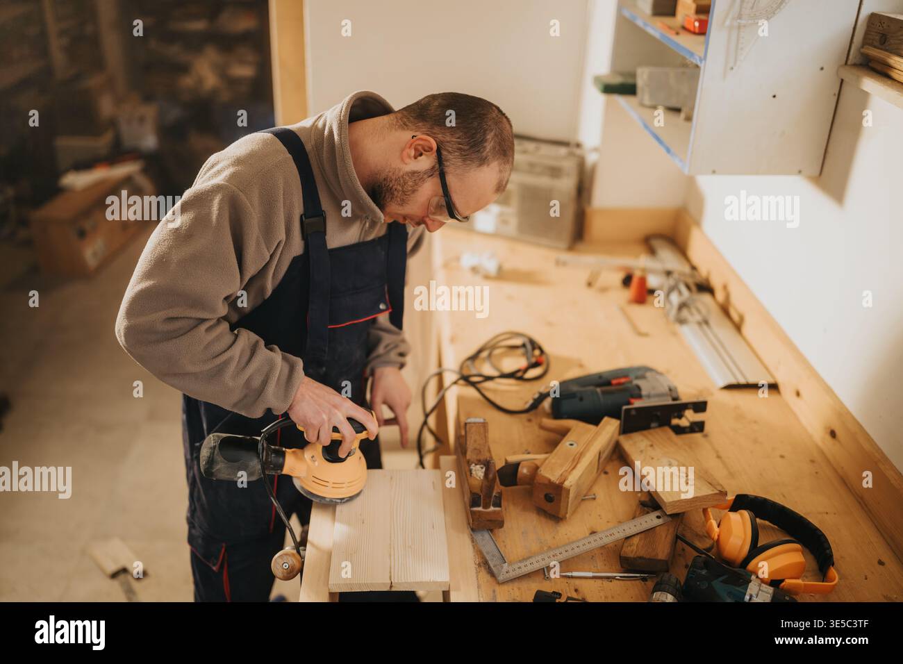 Carpenter sanding wooden board in workshop using an electric sander on workbench Stock Photo