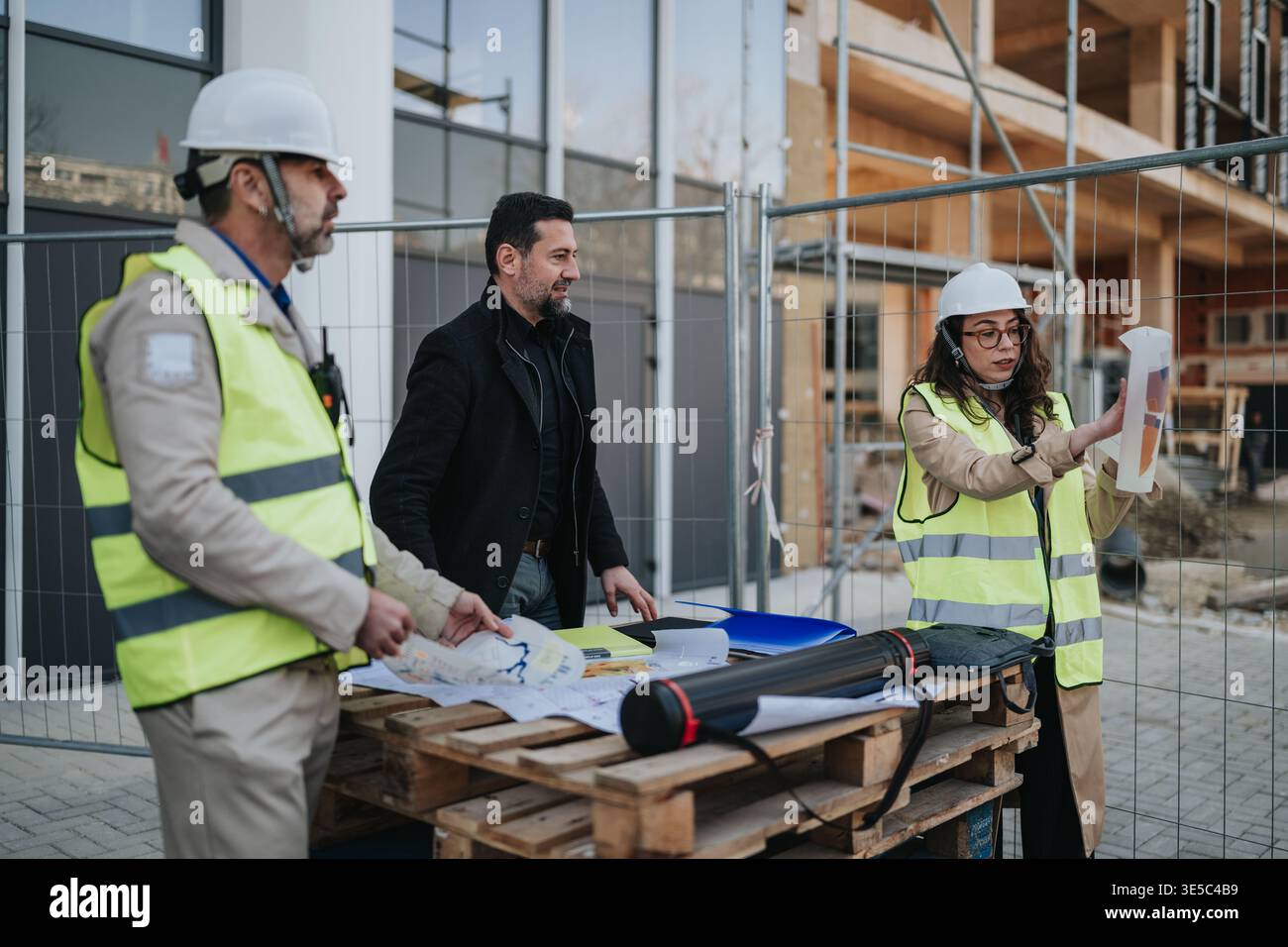 Construction engineers reviewing plans at an active building site with hard hats and high-visibility vests Stock Photo