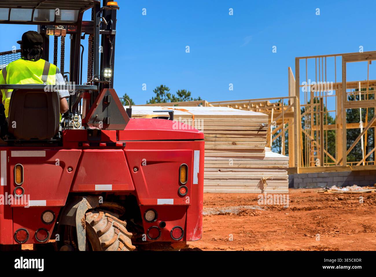 Forklift operator moves stacks of lumber on construction site where ...