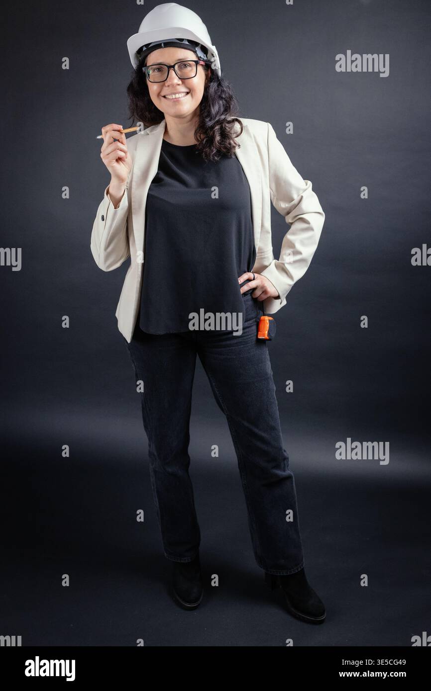 Smiling woman architect wearing hard hat and glasses holding a pencil, ready for work Stock Photo