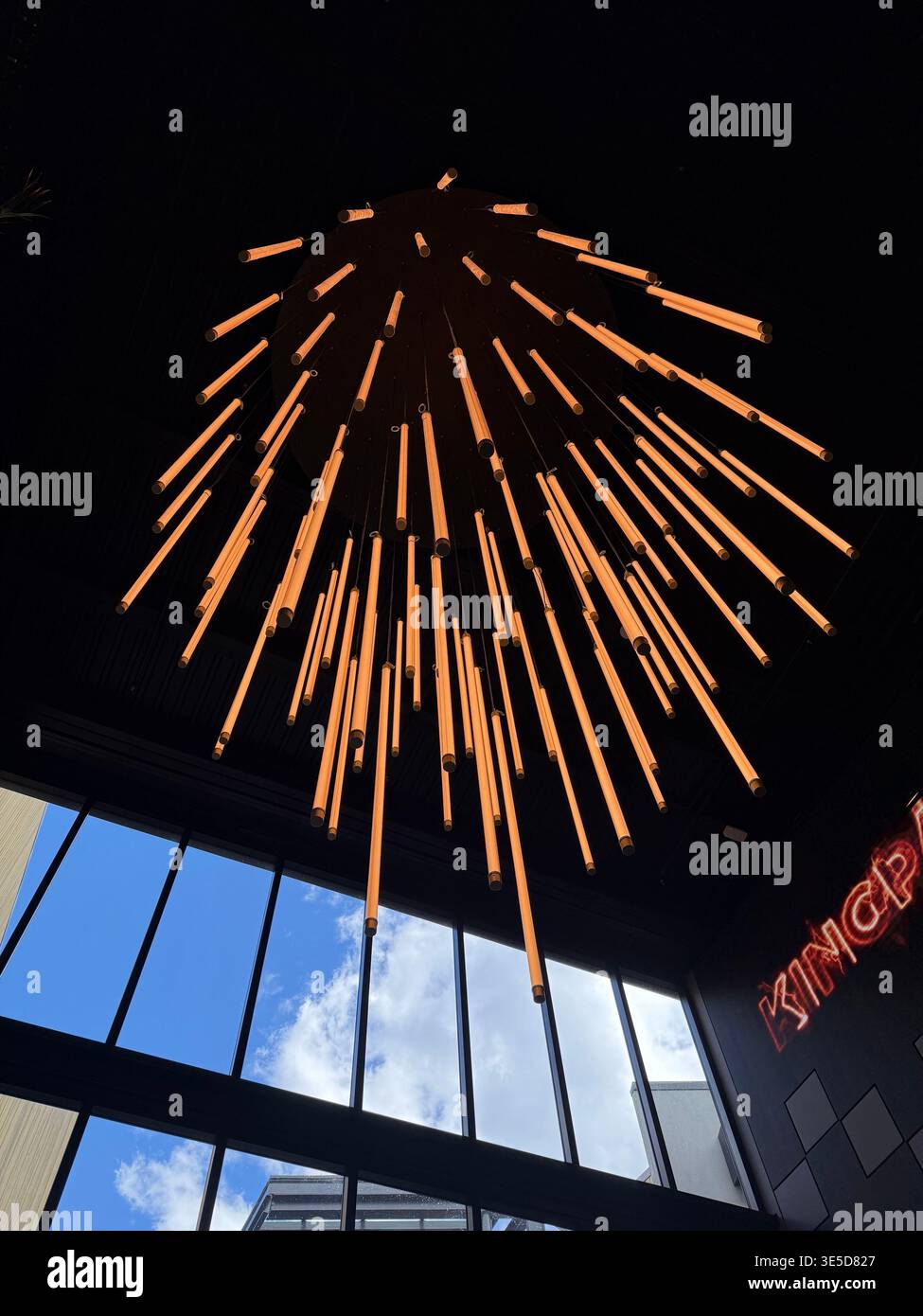 Large modern hanging light sculpture with glowing orange tubes, artistic chandelier - Smartphone Captured Stock Image
