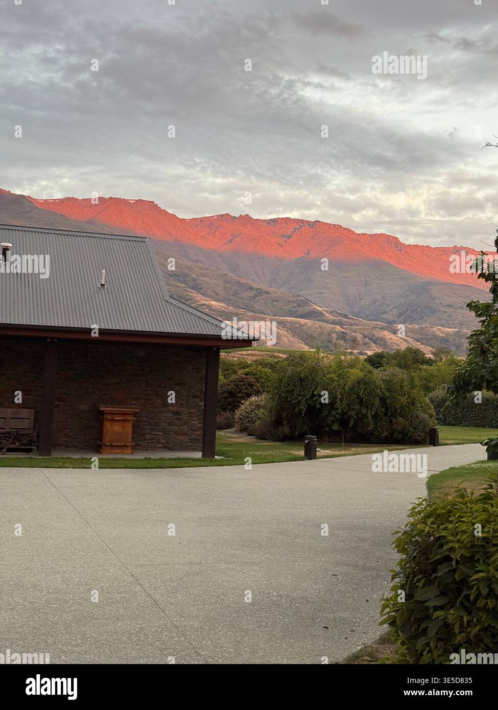 Stone building with dramatic red alpenglow on mountains at sunset, Cromwell, Central Otago, New Zealand - Smartphone Captured Stock Image