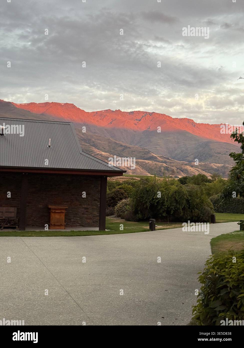 Stone building with dramatic red alpenglow on mountains at sunset, Cromwell, Central Otago, New Zealand - Smartphone Captured Stock Image