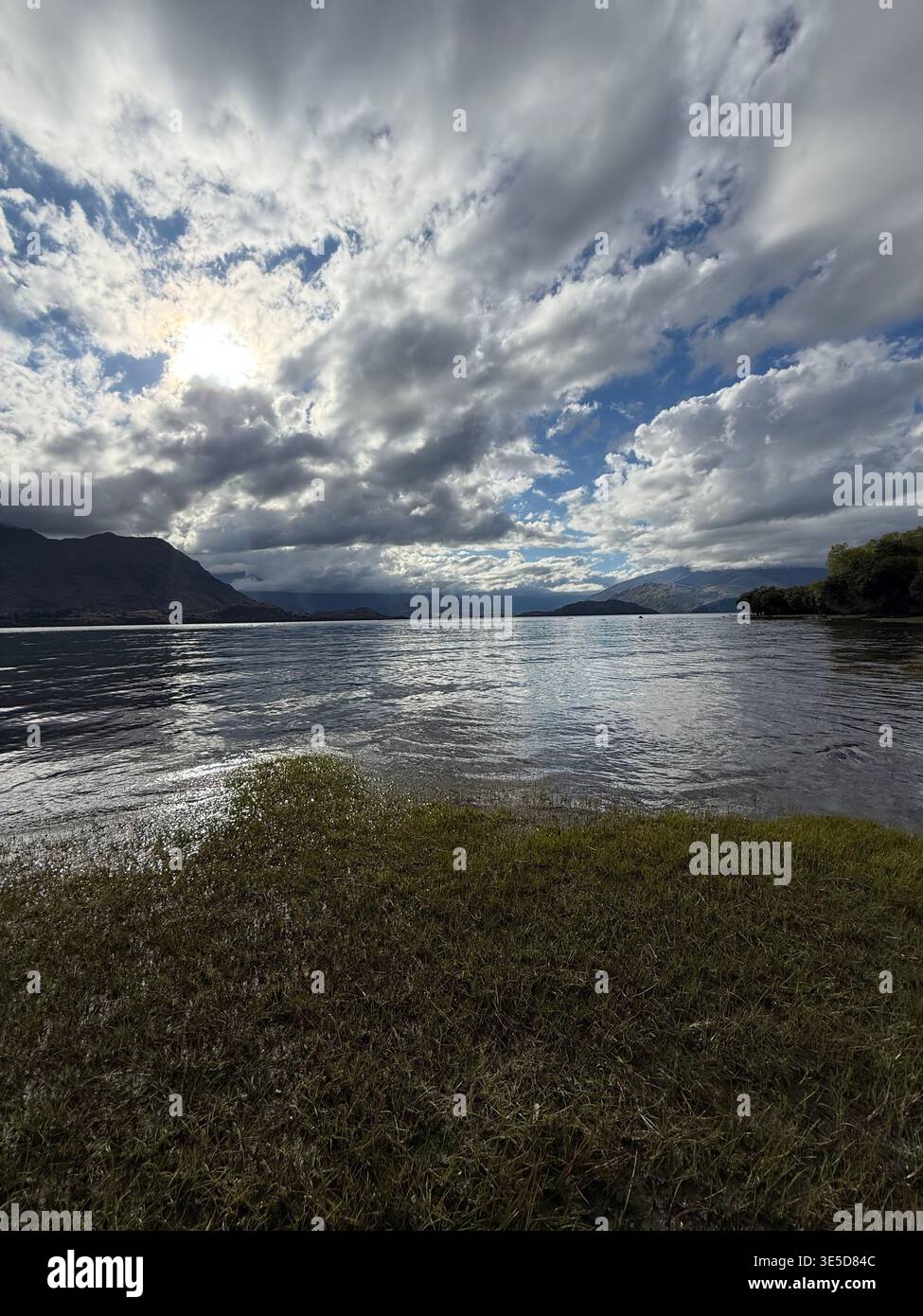 Dramatic cloudy sky over Lake Wanaka with bright sun breaking through, South Island, New Zealand - Smartphone Captured Stock Image