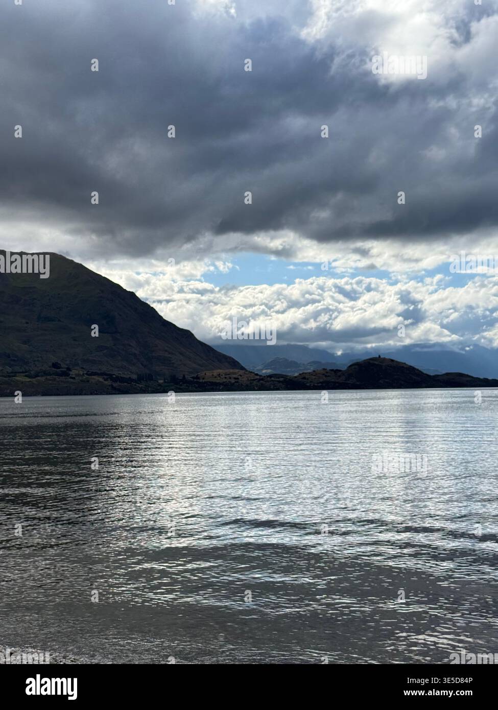 Dramatic cloudy sky over Lake Wanaka with bright sun breaking through, South Island, New Zealand - Smartphone Captured Stock Image