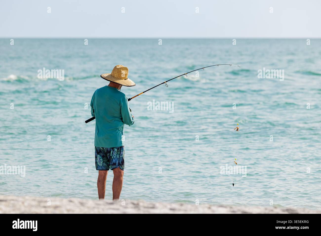Saltwater fisherman fishing from the beach. Man surf cast fishing from the shoreline of the Gulf of America, Florida. Stock Photo