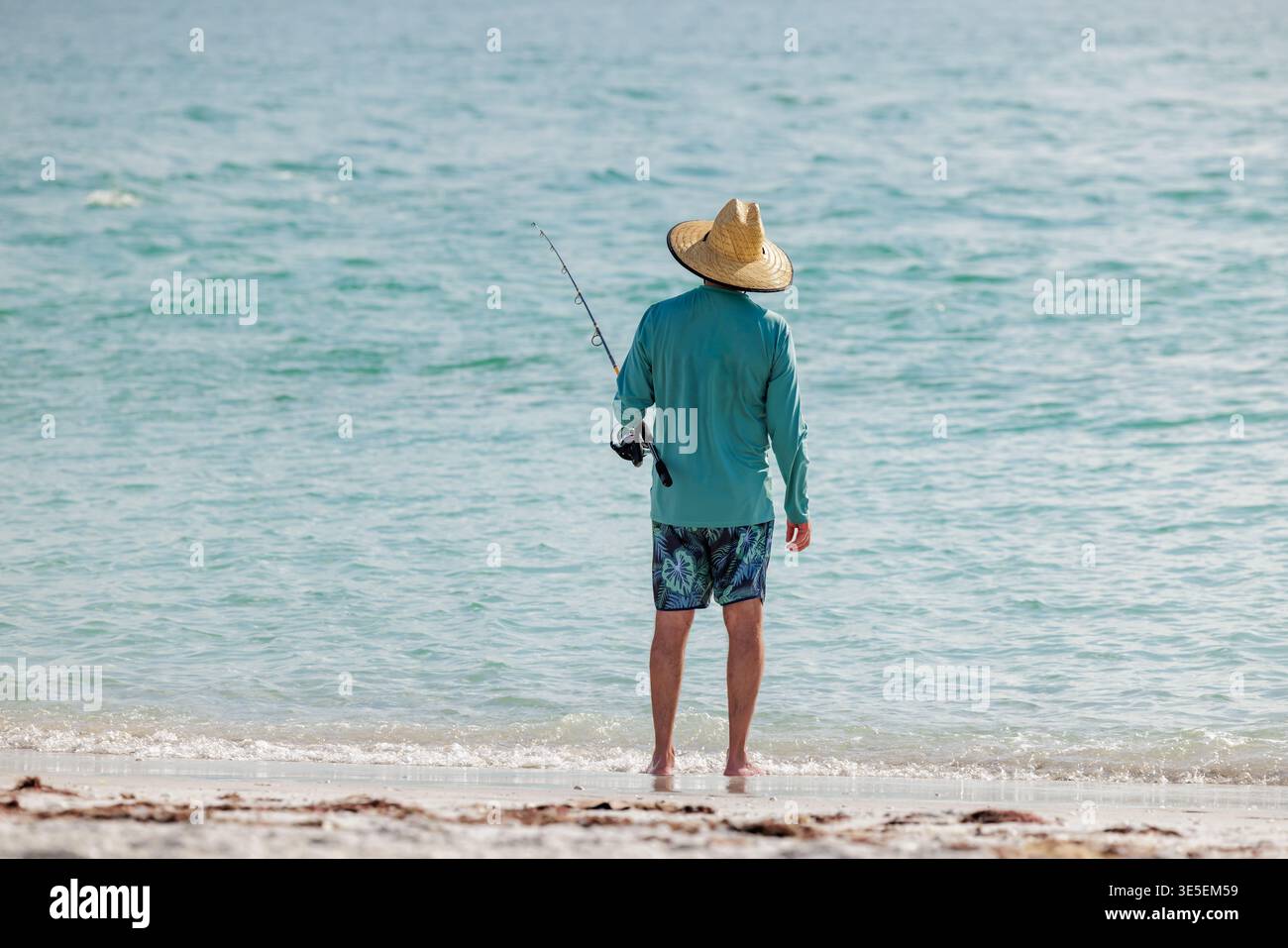 Saltwater fisherman fishing from the beach. Man surf cast fishing from the shoreline of the Gulf of America, Florida. Stock Photo