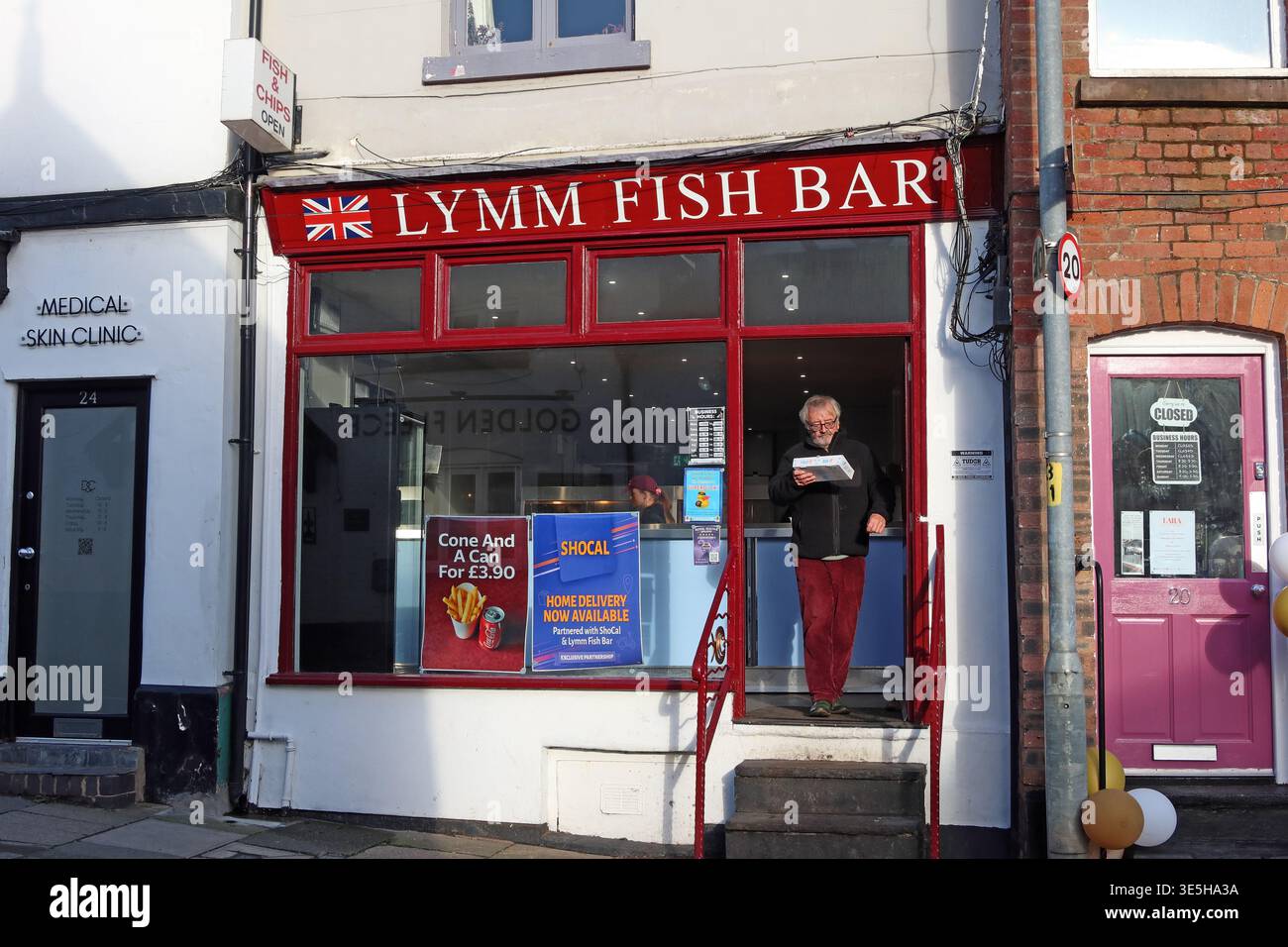 Customer emerges from Lymm Fish Bar, a traditional British chippy on The Cross in Lymm, Cheshire, England Stock Photo