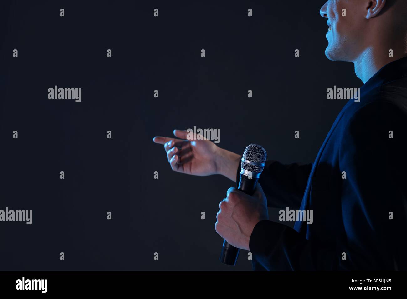 Happy presenter with microphone performing on dark background, closeup. Space for text Stock Photo