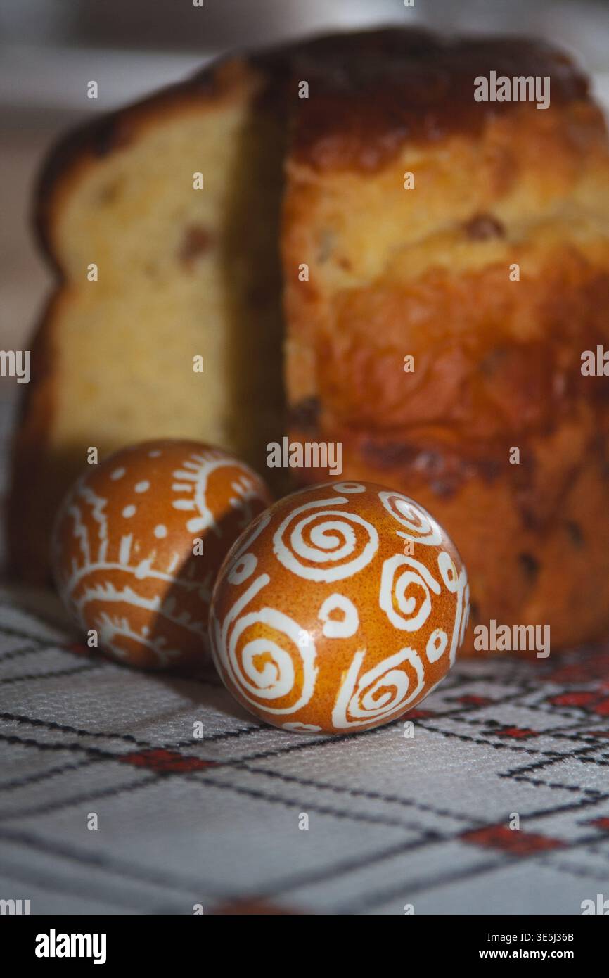 A festive Easter composition featuring two brown eggs decorated with white patterns and a sliced sweet Easter bread (paska) on a traditional embroider Stock Photo