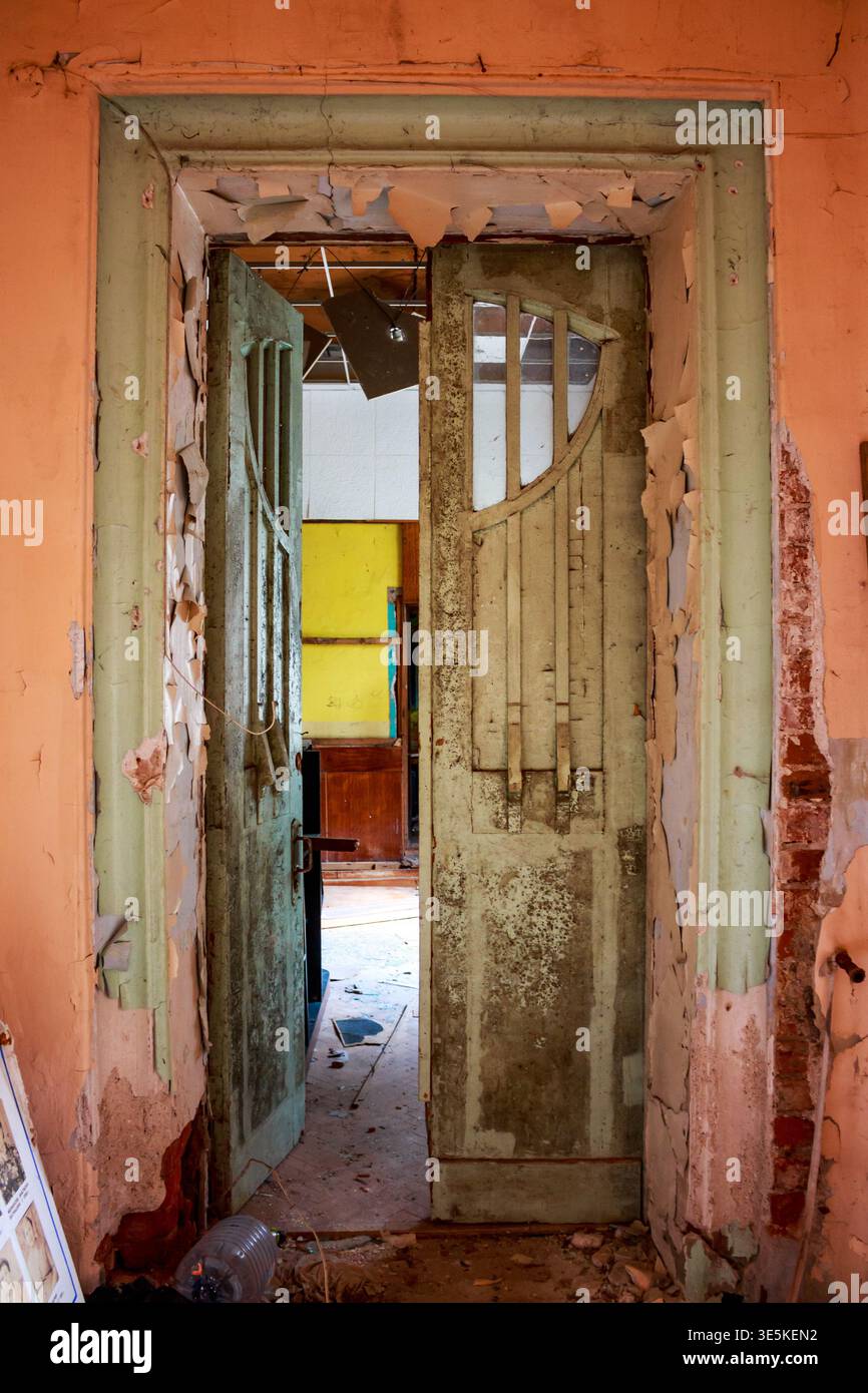 Decaying doorway with peeling paint and exposed brick opens into rooms with vibrant contrasting colors and debris strewn about Stock Photo