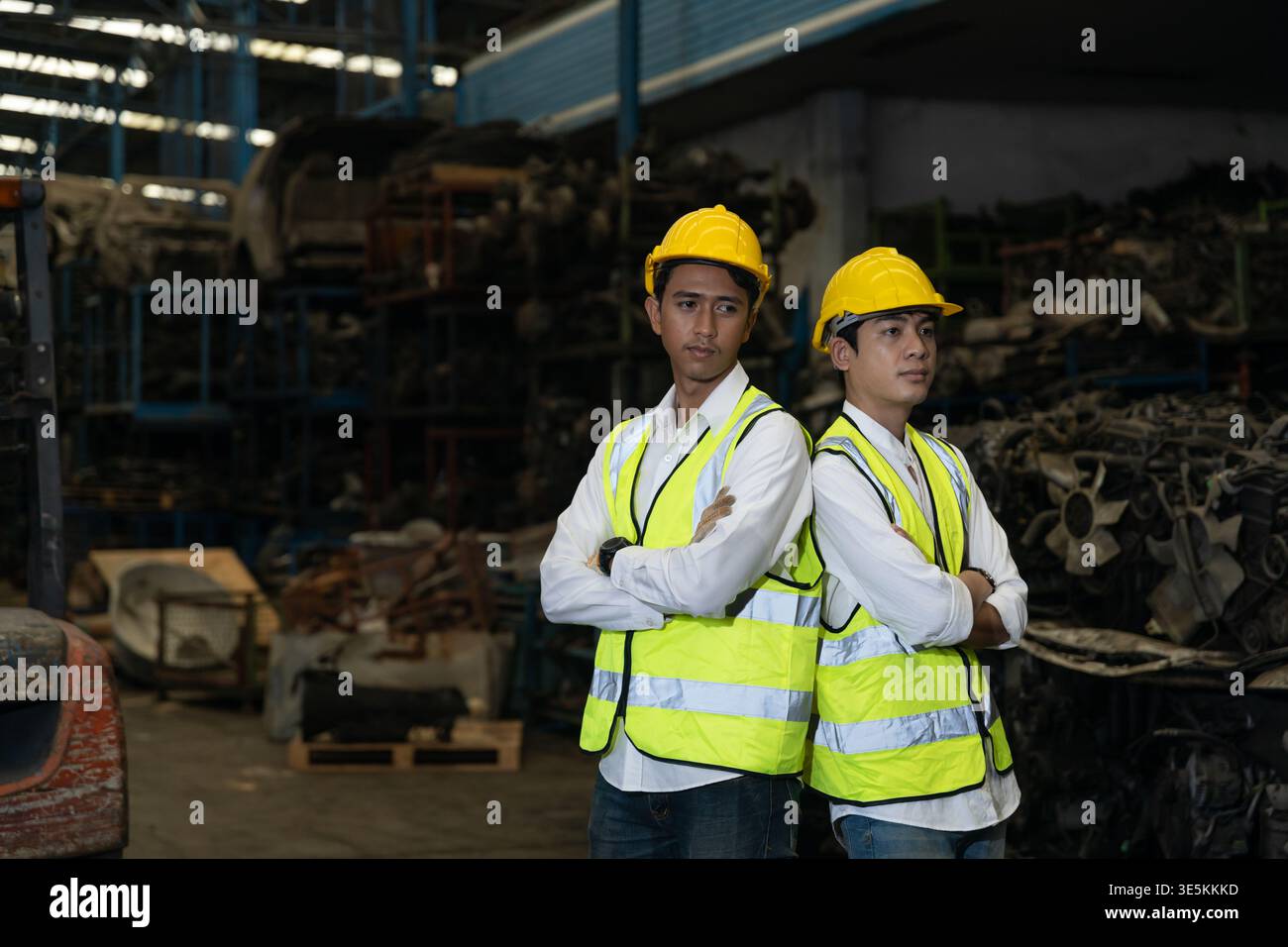 Two confident Asian industrial workers standing back to back in warehouse wearing safety gear Stock Photo