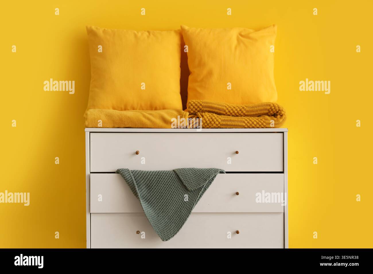 Pillows with folded blankets on commode near yellow wall Stock Photo