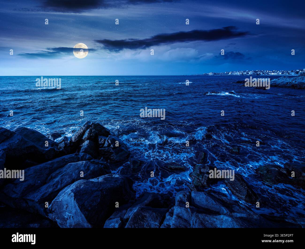 sea coast with stones and boulders at night. view of beach with rock in seaweed. full moon over dynamic cloudscape on the sky above horizon. mysteriou Stock Photo