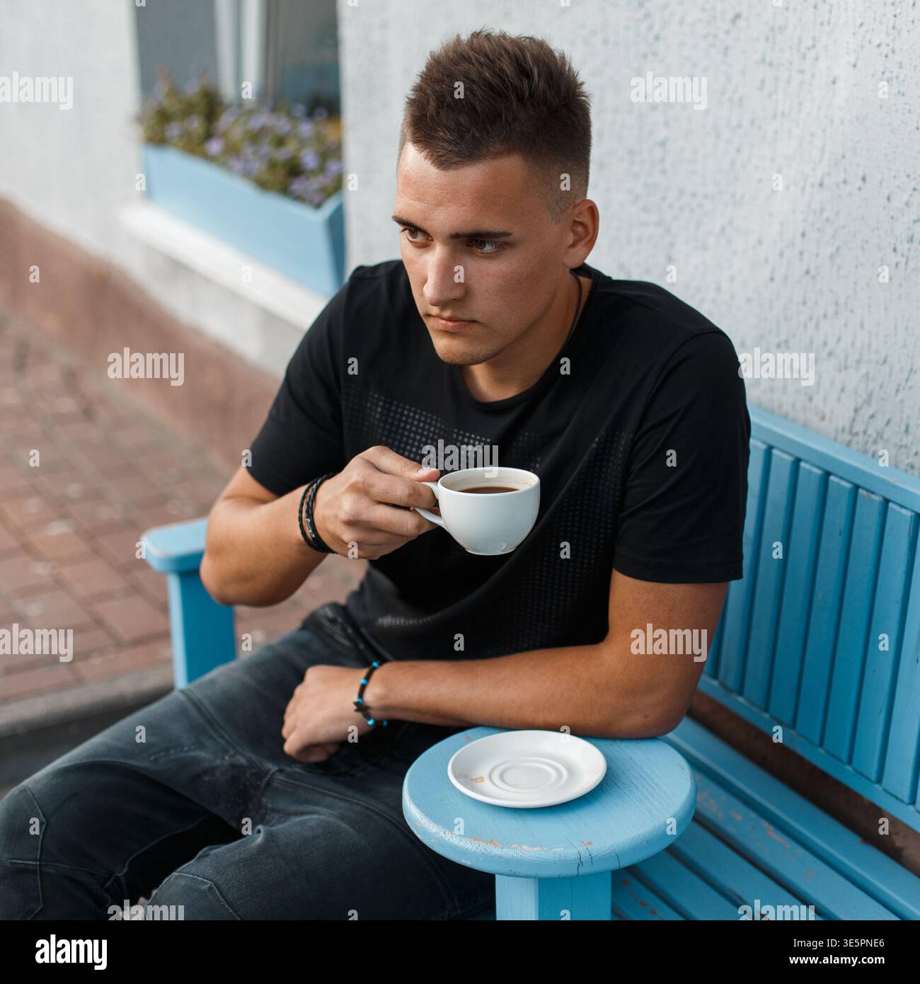 Handsome young man sitting outdoors in a cafe and drinking coffee Stock Photo