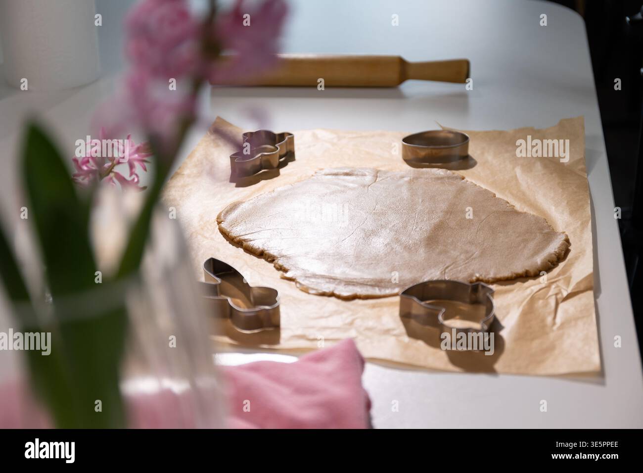Springtime baking happens in the kitchen with rolled gingerbread dough prepared for Easter cookies. Cookie cutters shaped like bunnies and eggs are ready for use. Flowers add color to the scene. Stock Photo