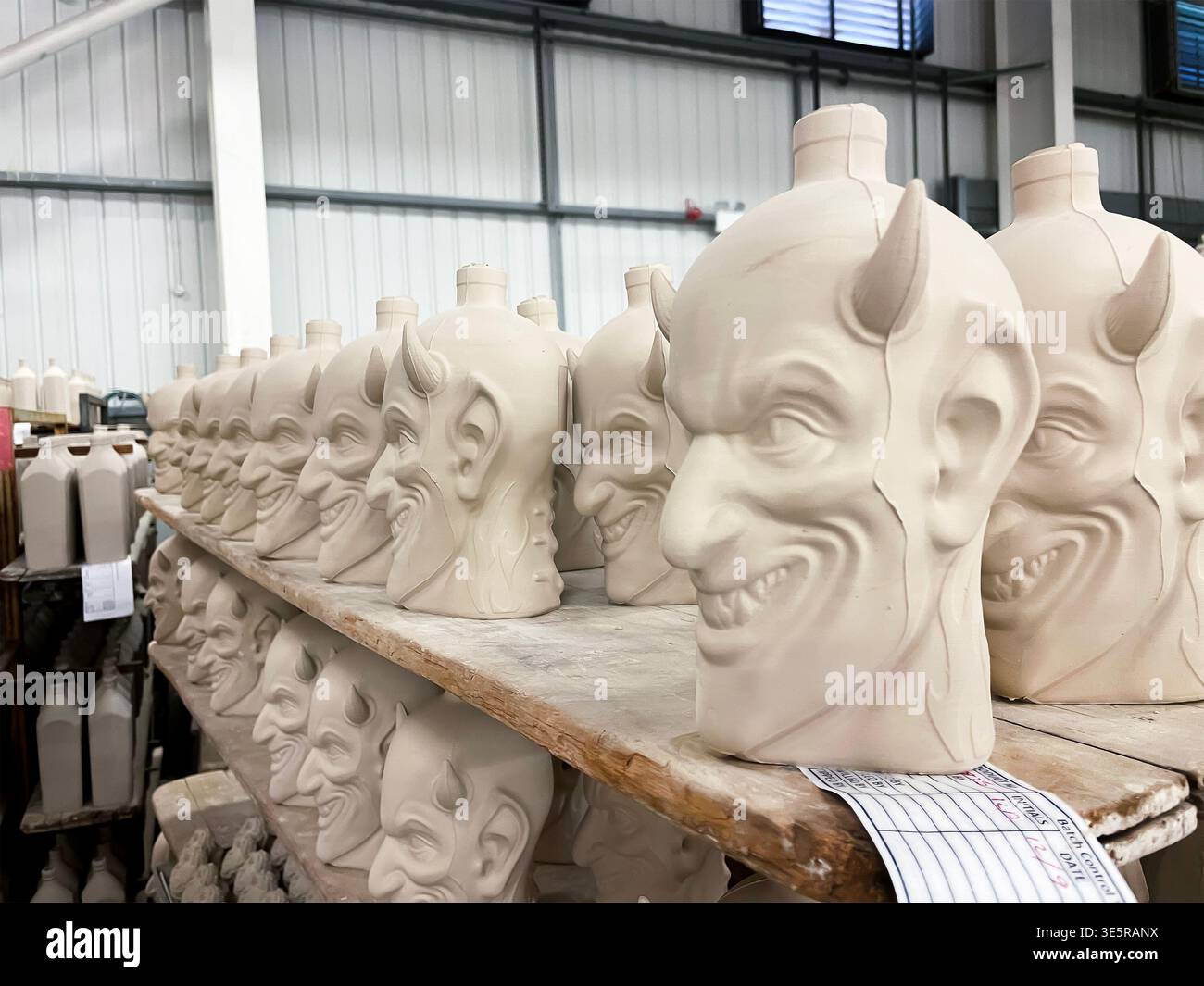 Rows of ceramic devil shaped whiskey decanters drying on wooden shelves inside a pottery factory in Stoke on Trent - Smartphone Captured Stock Image
