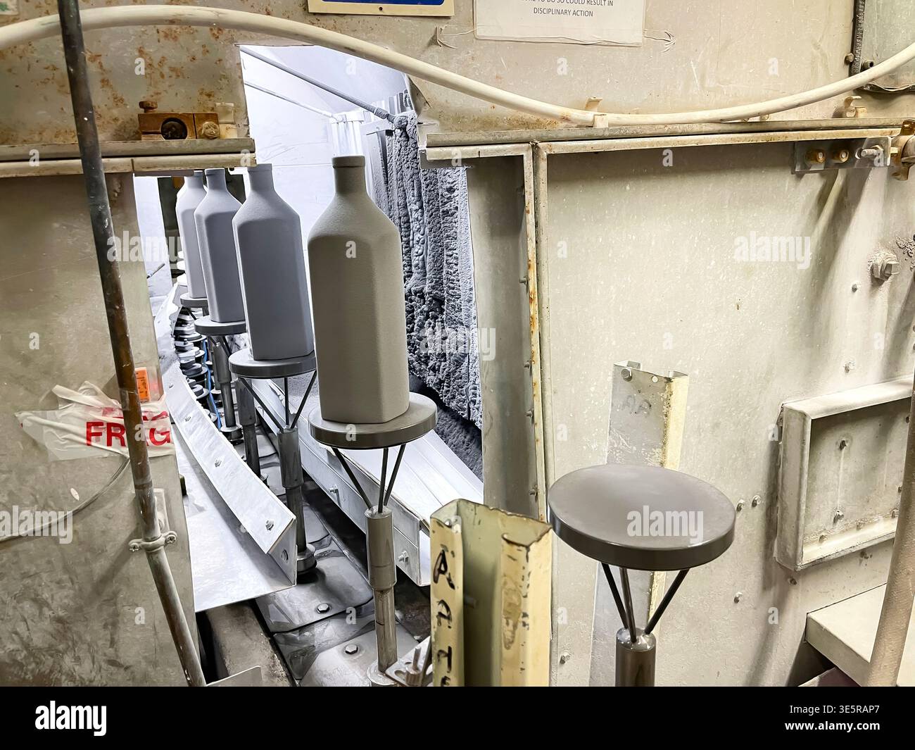 Industrial production line with ceramic bottles moving through a processing unit in a manufacturing facility - Smartphone Captured Stock Image