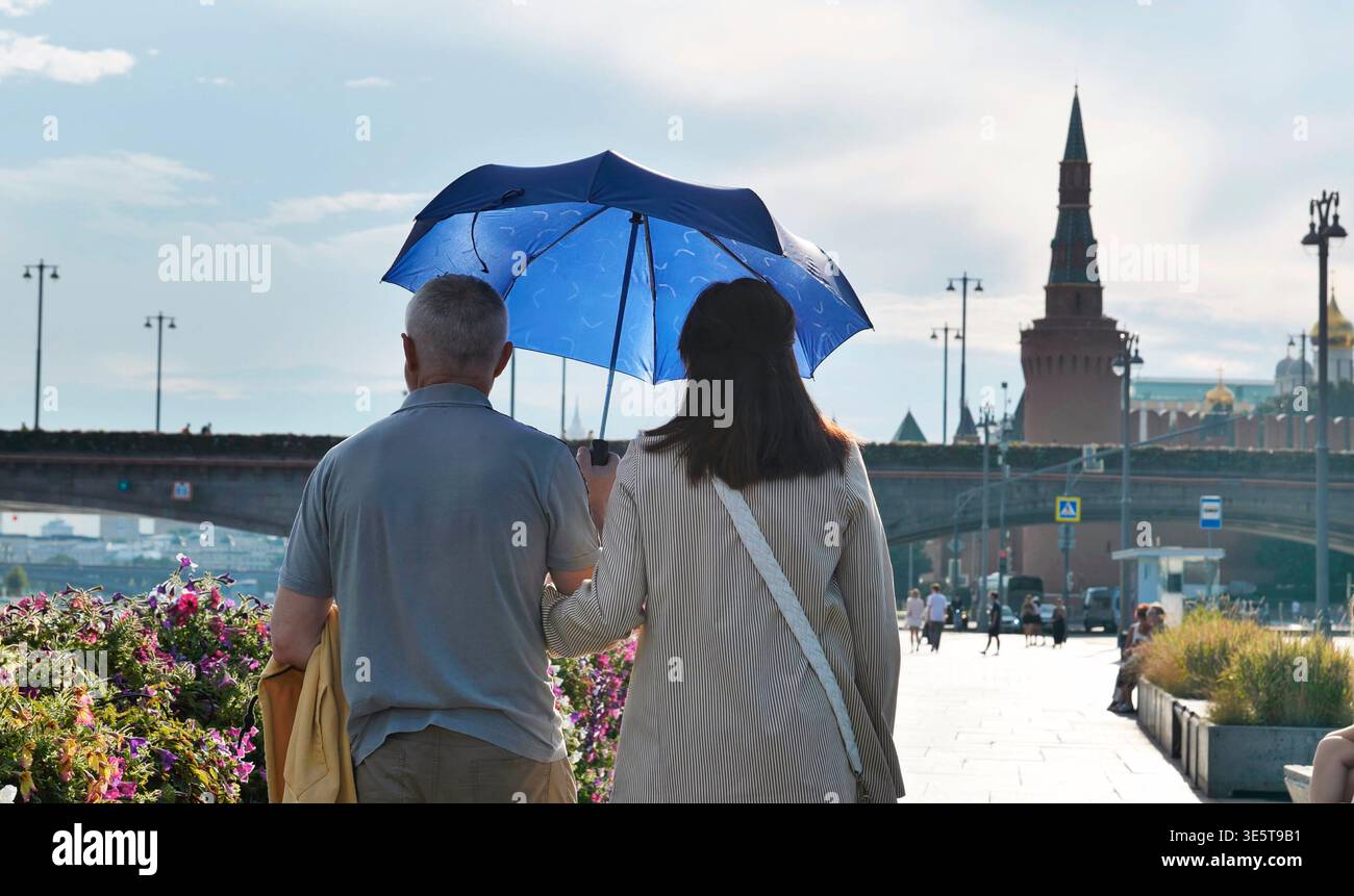 Senior couple walking with umbrella on Moscow embankment, enjoying sunny day Stock Photo