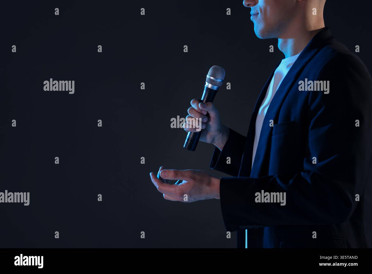 Presenter with microphone performing on dark background, closeup. Space for text Stock Photo