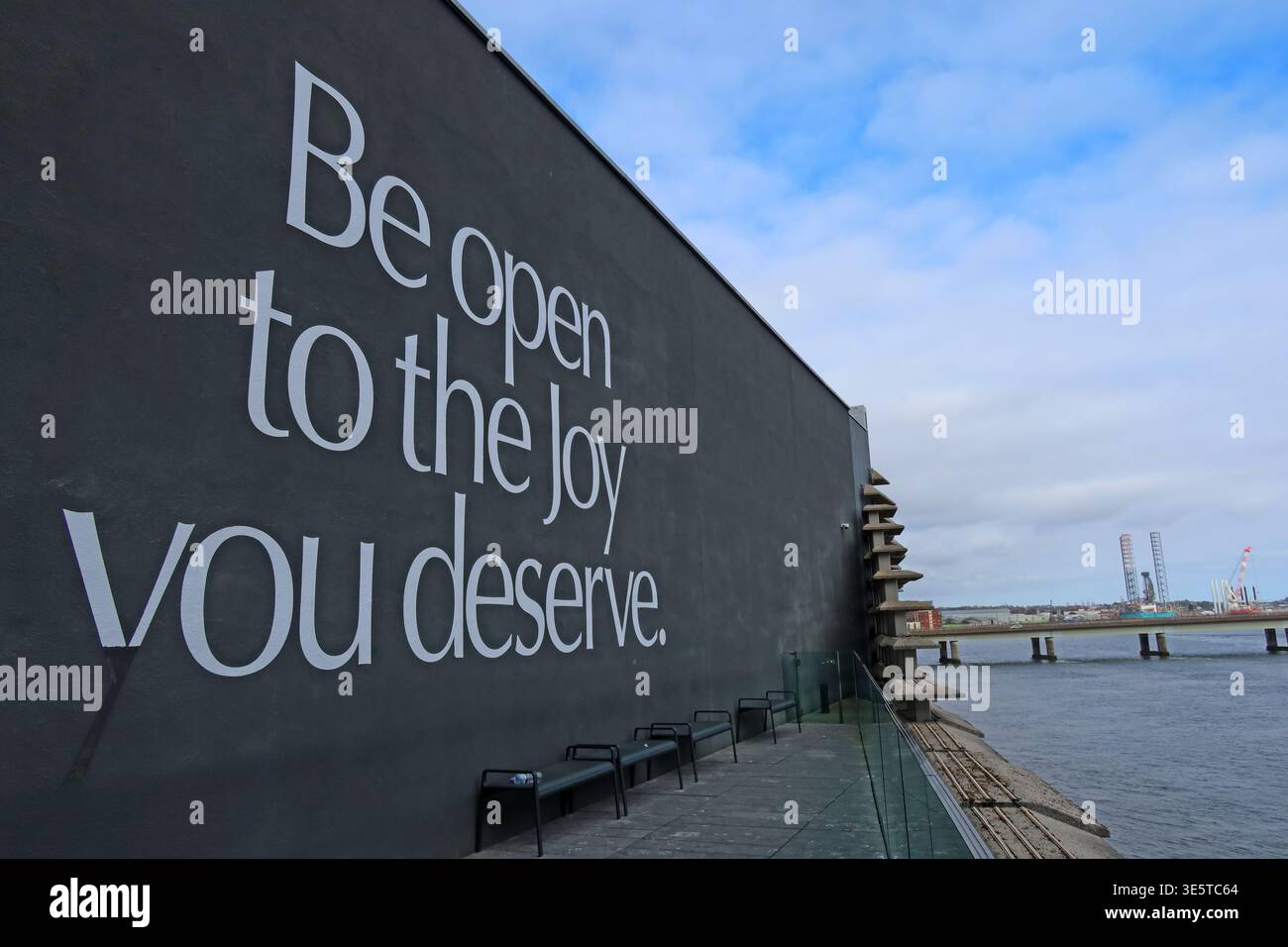 Large exterior wall text at V&A Dundee on Dundee waterfront, Scotland, reading “Be open to the joy you deserve” beside the River Tay. Stock Photo
