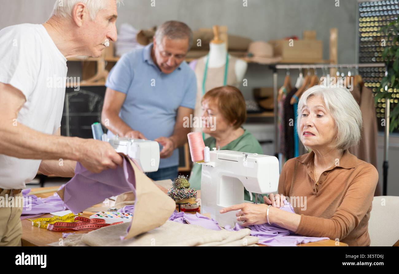 Some people communicate and discuss pattern, while others sew using sewing machine at lesson Stock Photo