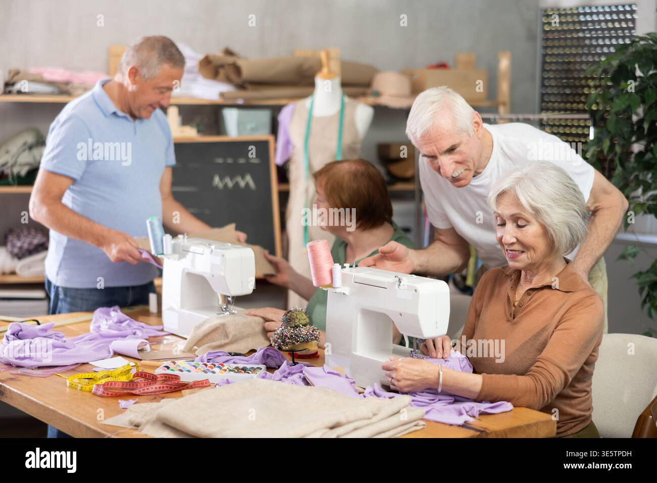 Some people communicate and discuss pattern, while others sew using sewing machine at lesson Stock Photo