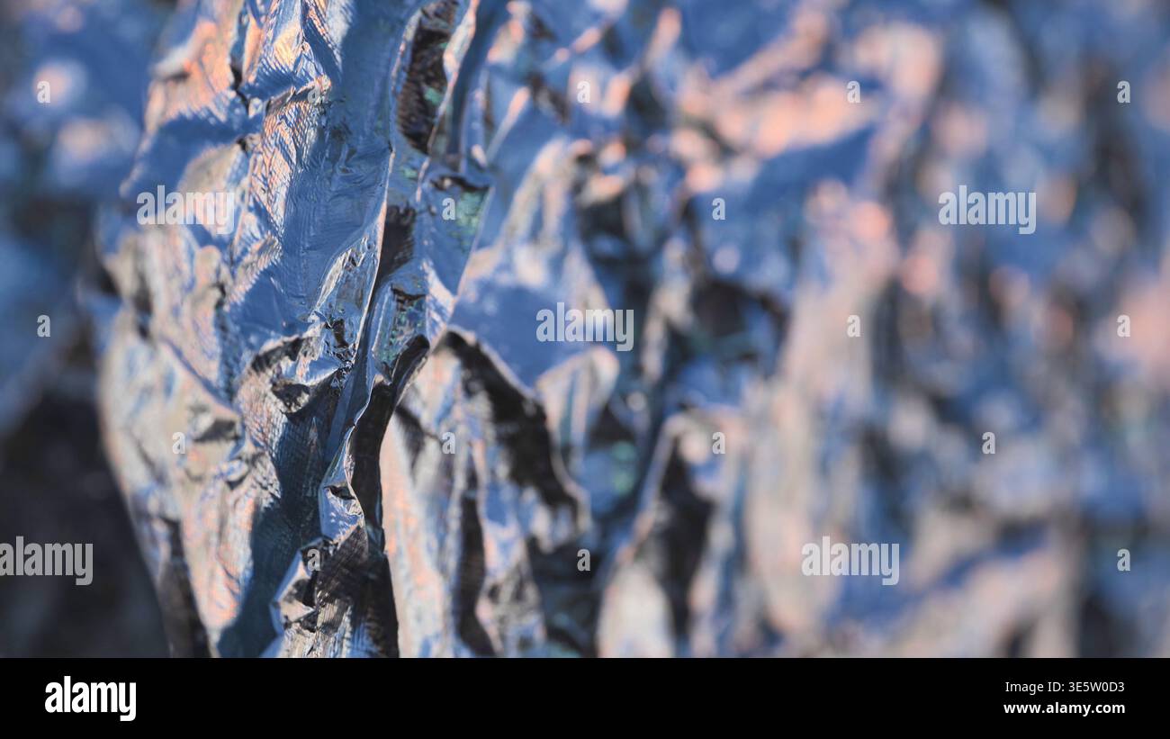 Crumpled metallic foil surface creating an iridescent abstract texture background Stock Photo