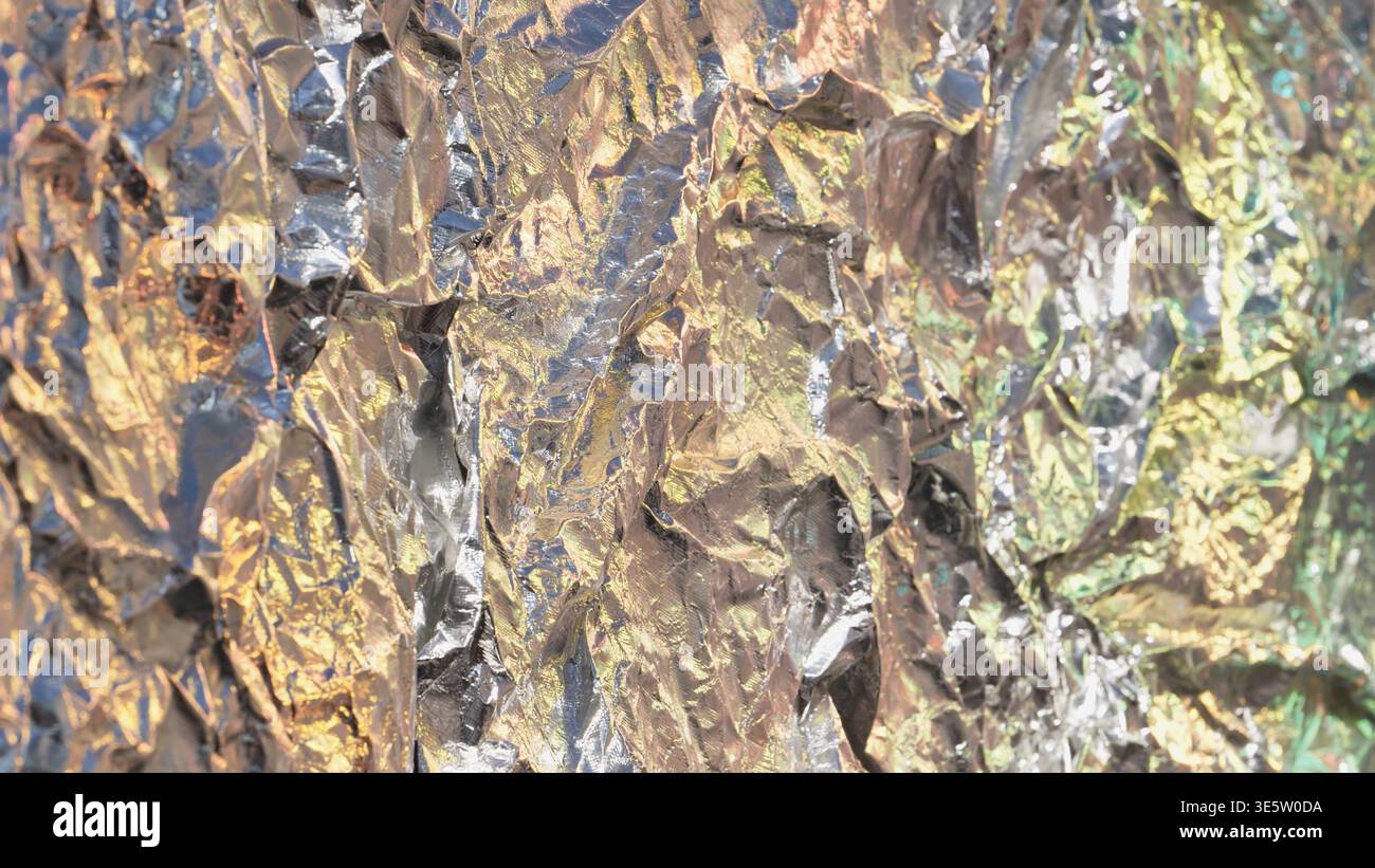 Crumpled aluminum foil surface reflecting metallic colors and abstract light textures Stock Photo