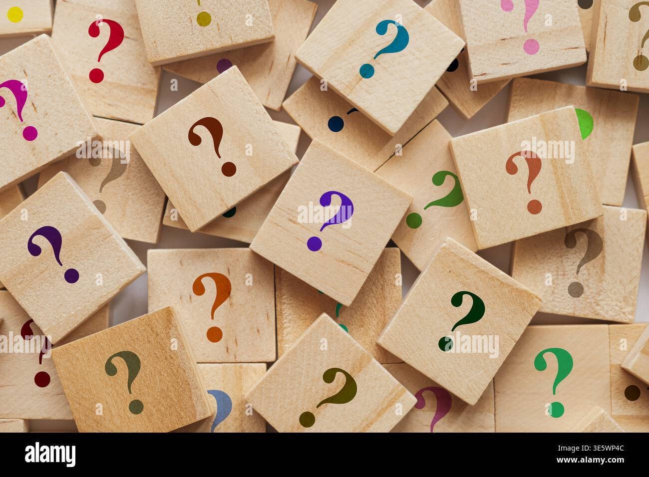 Too many wooden cubes with colorful question marks. Scattered blocks on blurred background symbolize curiosity and problem solving Stock Photo