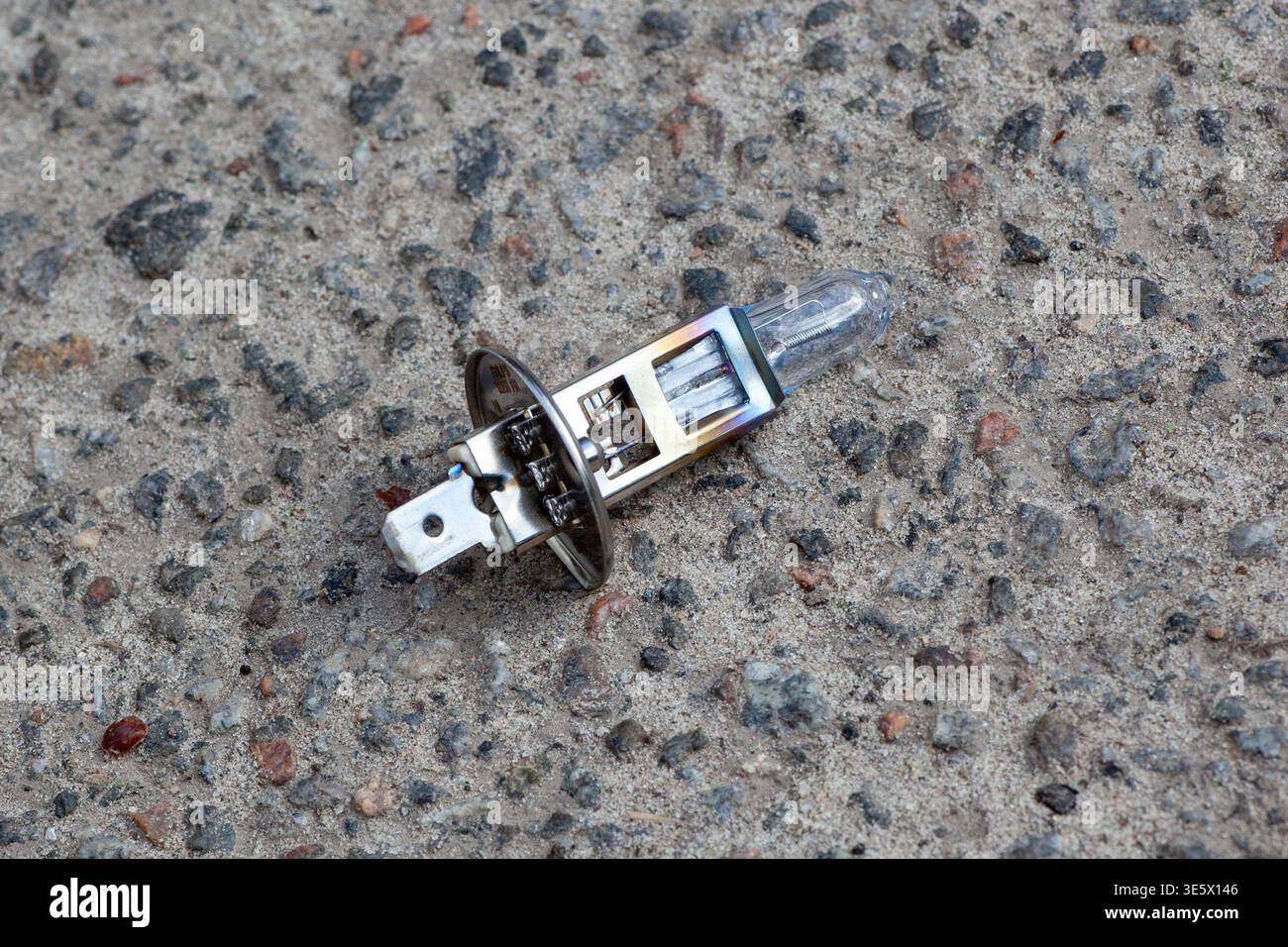 A lampa dlya fary lies on a rough, gray surface near a road. The sun is shining, and the area seems busy with potential traffic. Stock Photo