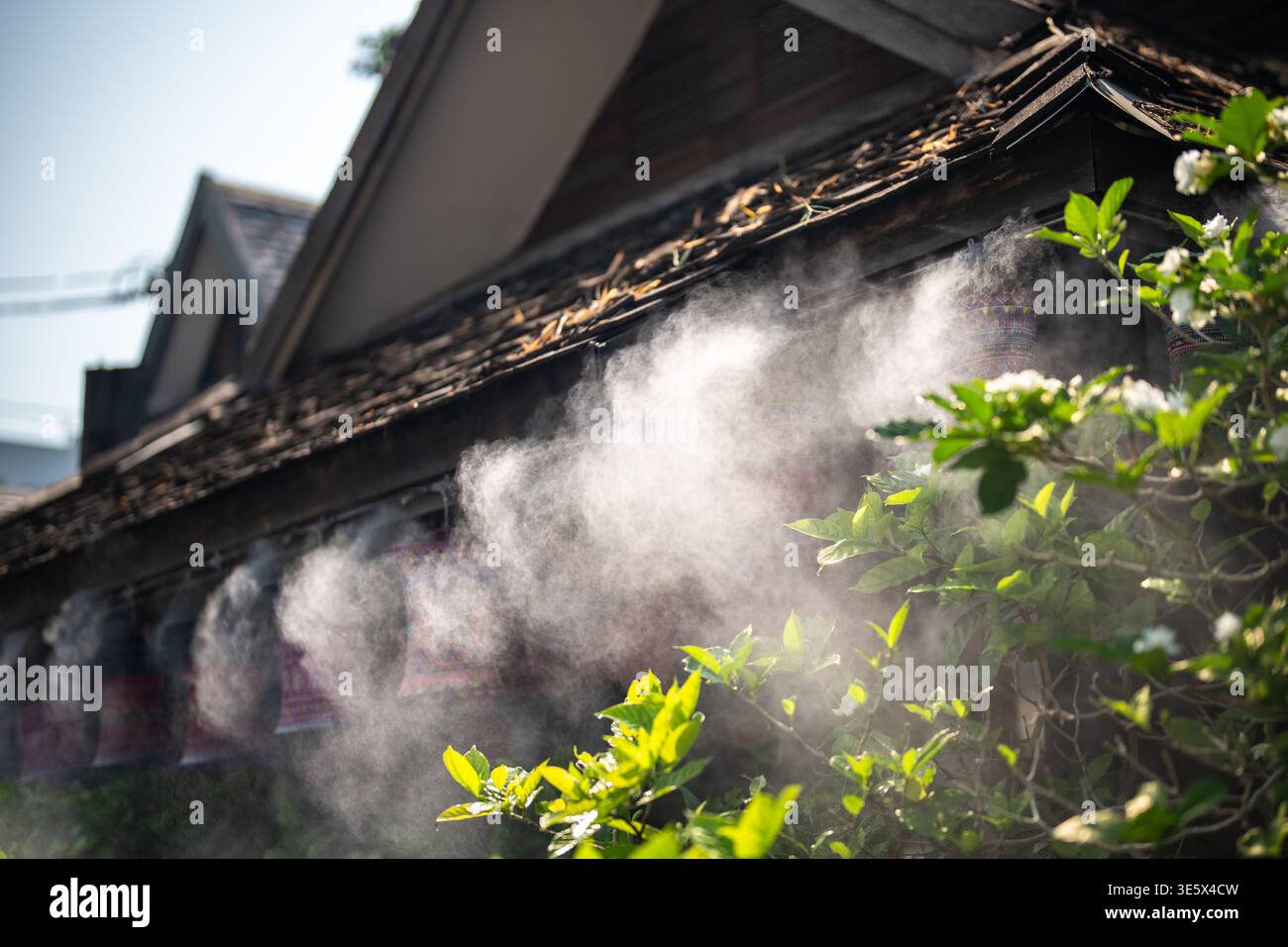 Refreshing mist spraying outside house from roof on hot summer day, water vapor spraying technology. Stock Photo