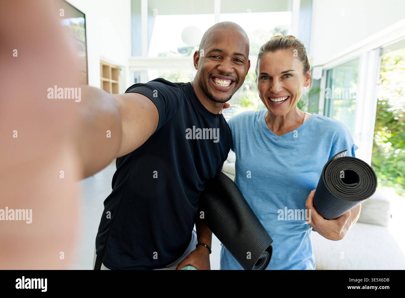 Couple in athletic shirts posing while taking phone selfie at home holding yoga mats water bottle Stock Photo