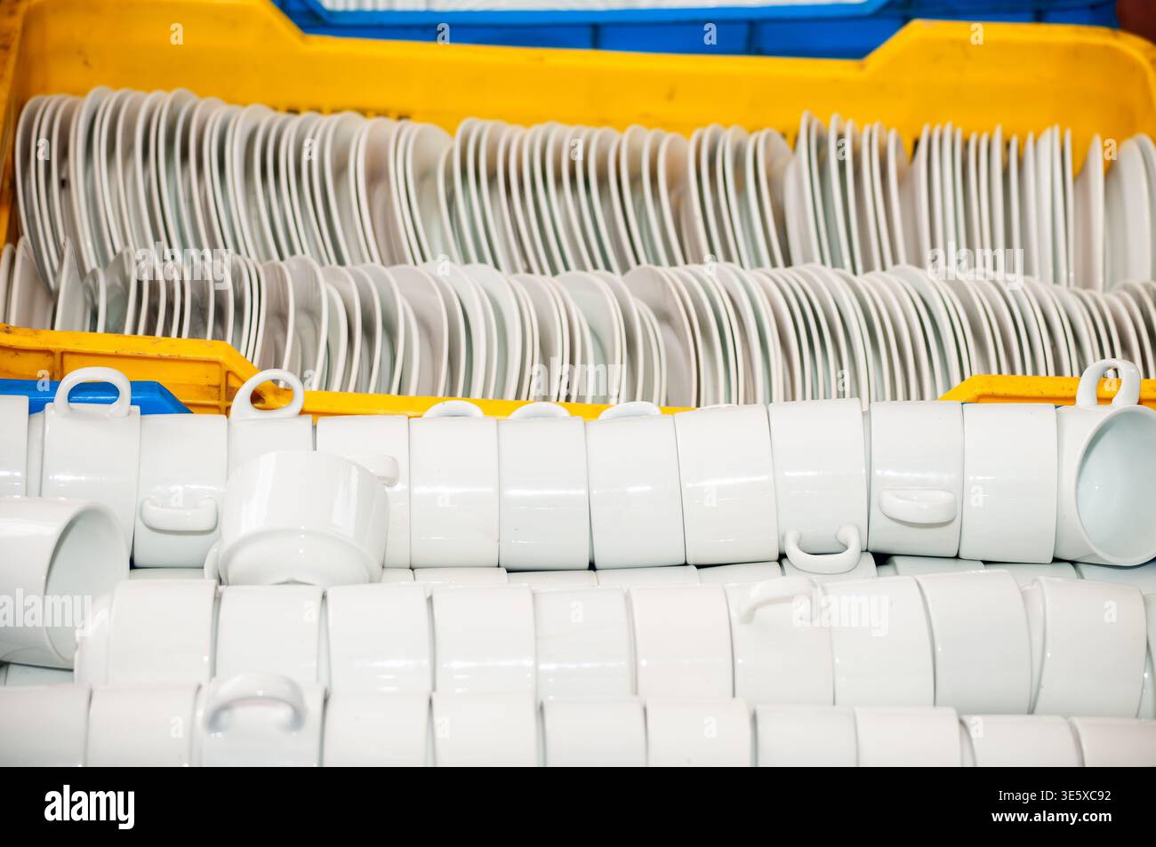 Stacked white ceramic cups and plates in plastic crates Stock Photo