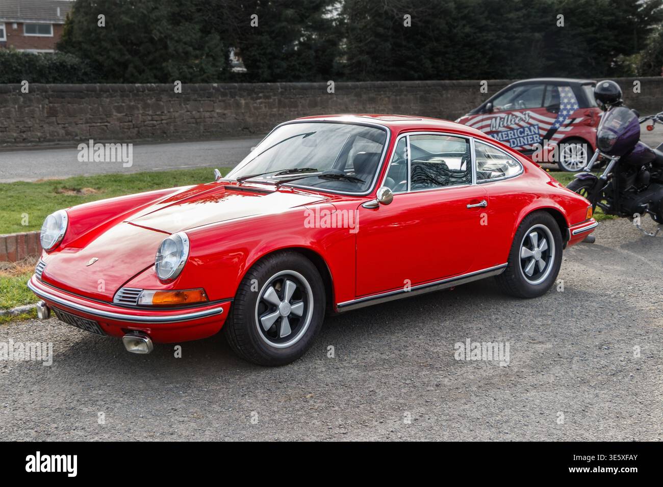 A vintage red Porsche 911 coupe parked on gravel with its distinctive round headlights and Fuchs style wheels during an outdoor car event Stock Photo