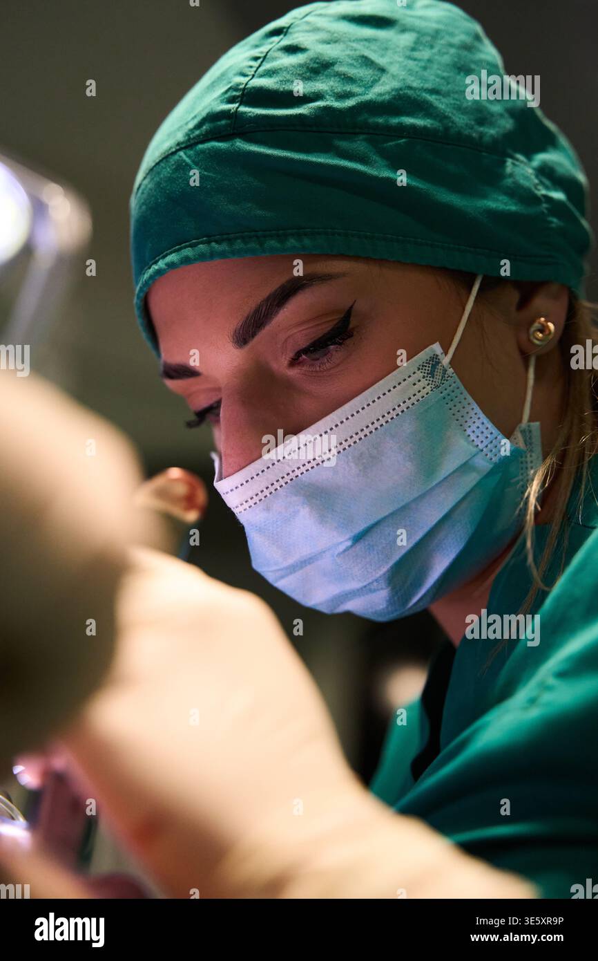 Focused female surgeon wearing surgical mask and cap performing a ...