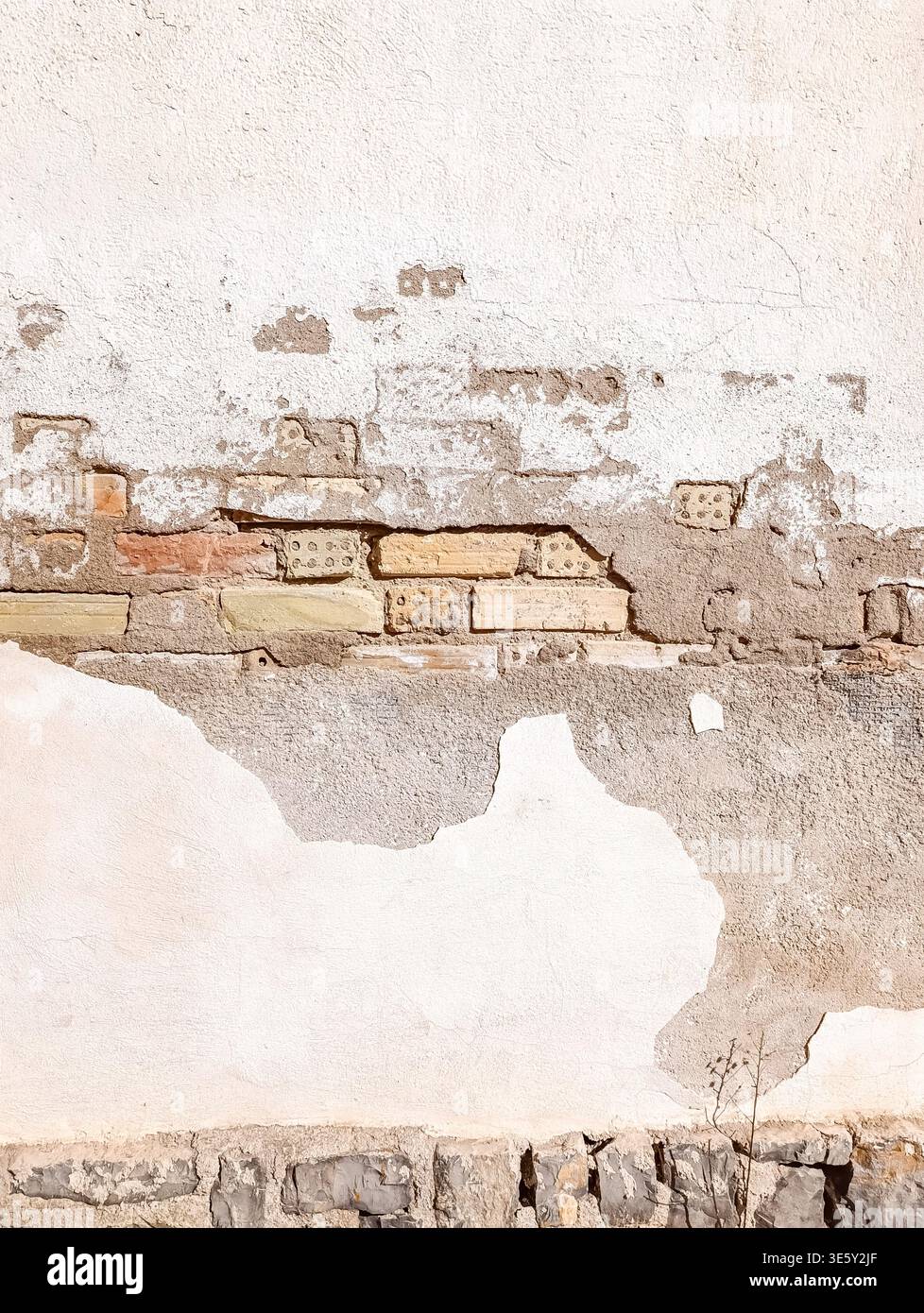 Peeling White Painted Wall with Exposed Old Bricks in Sunlight Stock Photo