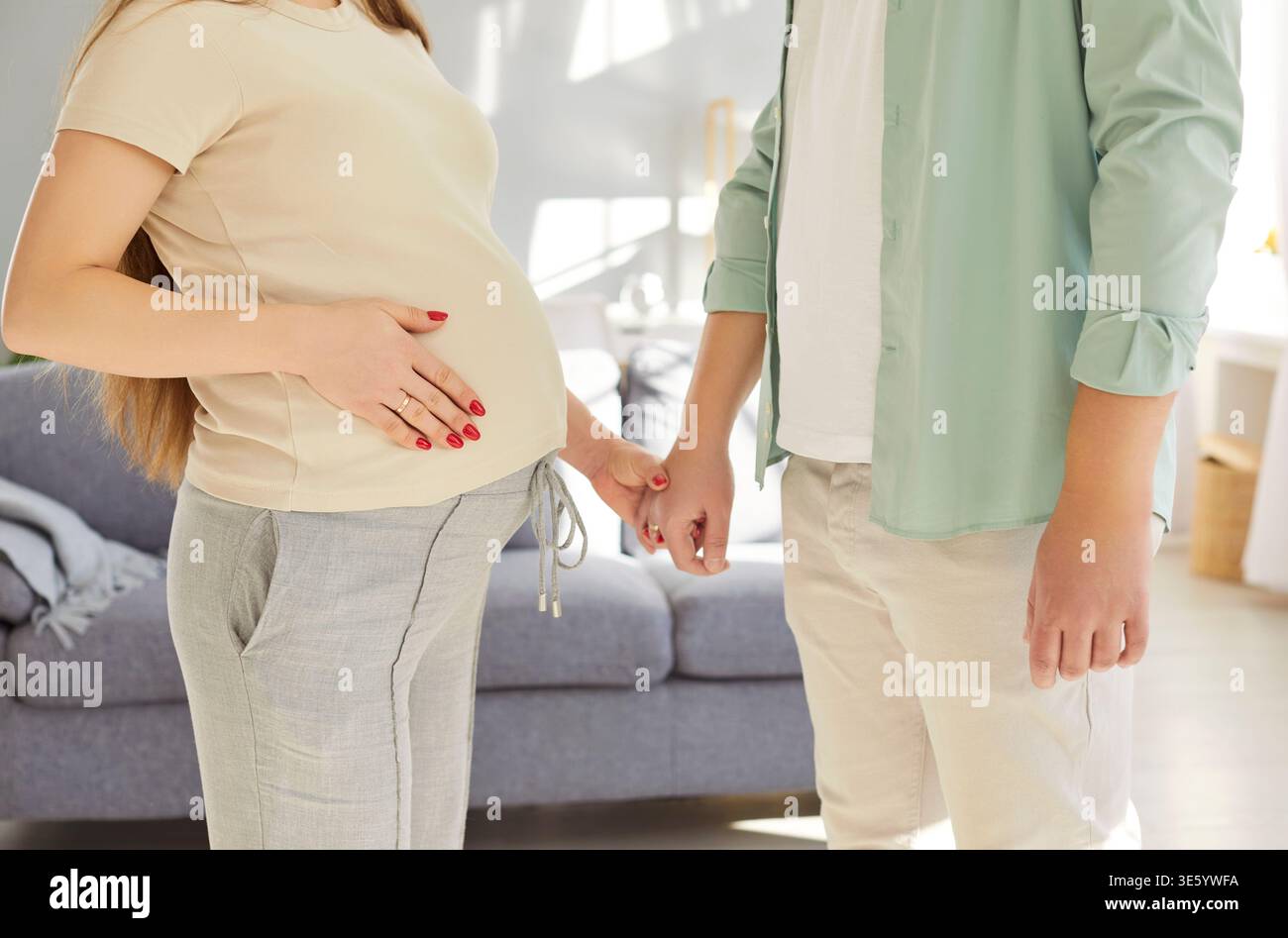 Happy young couple standing together at home, holding hands, supporting each other during pregnancy. Stock Photo
