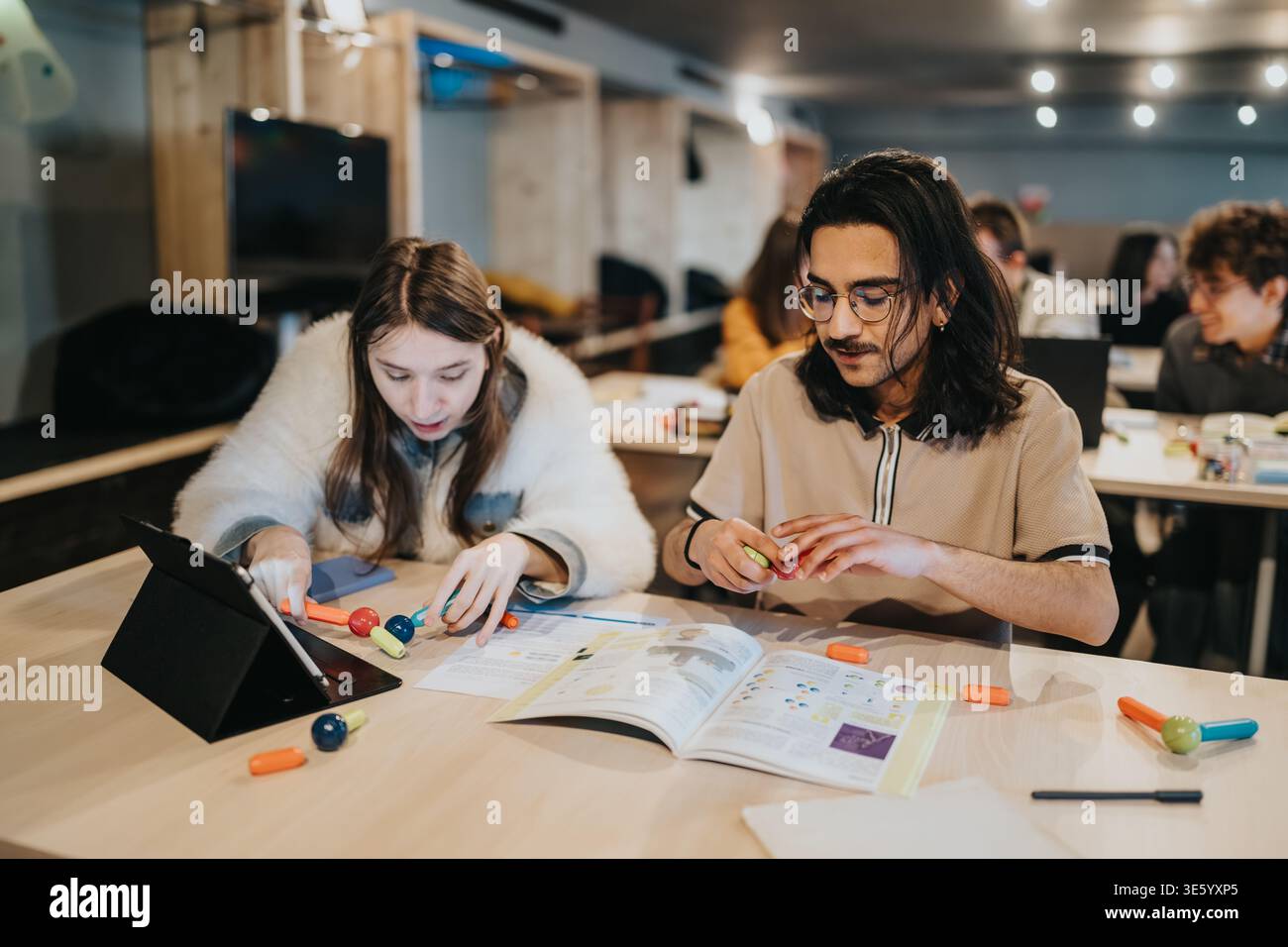 Two students collaborating on a study project with tablet and textbooks in a modern classroom Stock Photo