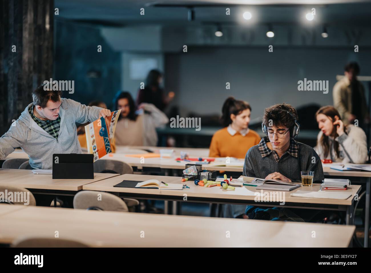 Students studying together in a shared classroom using books, tablets and headphones Stock Photo