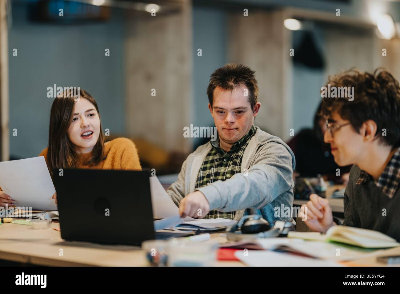 Three students studying together around a laptop in a collaborative classroom setting Stock Photo